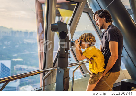 Dad and son are looking at Kuala lumpur cityscape. Use binoculars. Panoramic view of Kuala Lumpur city skyline evening at sunset skyscrapers building in Malaysia. Traveling with kids concept 101390844