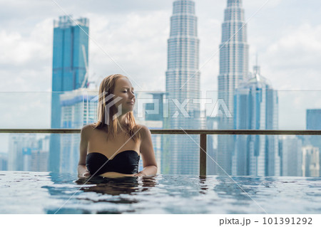 Young woman in outdoor swimming pool with city view in blue sky 101391292