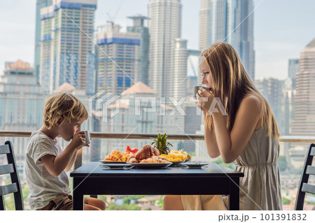Happy family having breakfast on the balcony. Breakfast table with coffee fruit and bread croisant on a balcony against the backdrop of the big city Happy family having breakfast on the balcony. Breakfast table with coffee fruit and bread croisant on a balcony against the backdrop of the big city 101391832