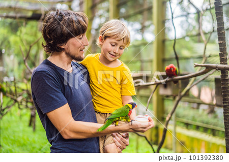 Dad and son feed the parrot in the park. Spending time with kids concept 101392380