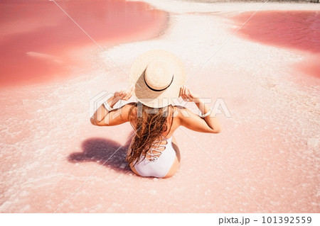 A woman traveler looks at an amazing pink salt lake. He sits with his back in a bathing suit and holds his hat in his hands. Wanderlust travel concept 101392559