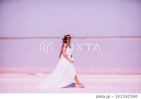 Woman in pink salt lake. She walks in a white long dress and hat along the salty white shore of the lake. Wanderlust photo for memory 101392560