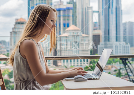Young woman is working on a laptop on her balcony overlooking the skyscrapers. Freelancer, remote work, work from home Young woman is working on a laptop on her balcony overlooking the skyscrapers. Freelancer, remote work, work from home 101392951