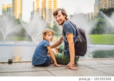 Dad and son tourists on background of fountain on the lake at night, near by Twin Towers with city on background. Kuala Lumpur, Malaysia Dad and son tourists on background of fountain on the lake at night, near by Twin Towers with city on background. Kuala Lumpur, Malaysia 101393308