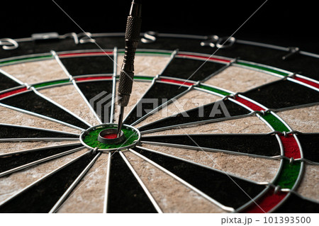 One dart hits the bull's eye of a dartboard on a black wooden background. Happy win and luck concept 101393500