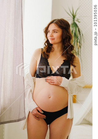 a beautiful pregnant woman in a black underwea and white shirt by the window 101395036