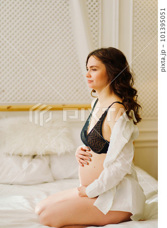 a slender pregnant woman in a black underwea and white shirt on the bed a slender pregnant woman in a black underwea and white shirt on the bed 101395051