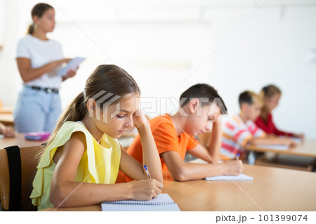 Interested diligent preteen schoolgirl writing exercises at lessons 101399074