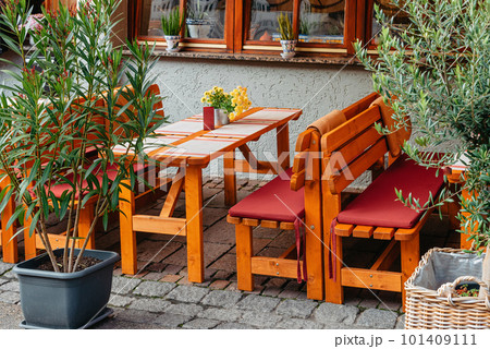 Street terrace of the coffee shop. Wooden tables next to the coffee shop behind green bushes. Coffee shop in the city center. Summer outdoor cafe with stone gray pavement green bushes in tubs sunny 101409111