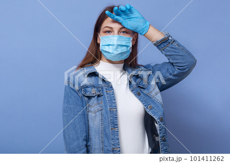 Portrait of sick exhausted poor lady putting hand on forehead, feeling unwell, having fever, being infected, staying home, being in self isolation, being in antibacterial mask. Covid19 concept. Portrait of sick exhausted poor lady putting hand on forehead, feeling unwell, having fever, being infected, staying home, being in self isolation, being in antibacterial mask. Covid19 concept. 101411262