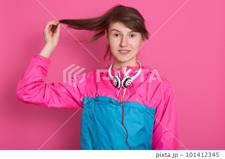 Horizontal shot of young pleased dark haired woman touching her brown long hair with raised hand while posing over pink studio wall, smiling slightly and looking directly at camera. People concept. Horizontal shot of young pleased dark haired woman touching her brown long hair with raised hand while posing over pink studio wall, smiling slightly and looking directly at camera. People concept. 101412345