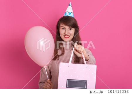Half length portrait of adorable girl, standing with present box and balloon. Gorgeous young woman with dark straight hair having fun on party holding gift, isolated over pink background. Holiday Half length portrait of adorable girl, standing with present box and balloon. Gorgeous young woman with dark straight hair having fun on party holding gift, isolated over pink background. Holiday 101412358
