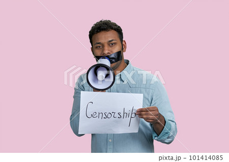 Young brown man with taped mouth holding megaphone and paper with censorship word. Isolated on pink background. 101414085