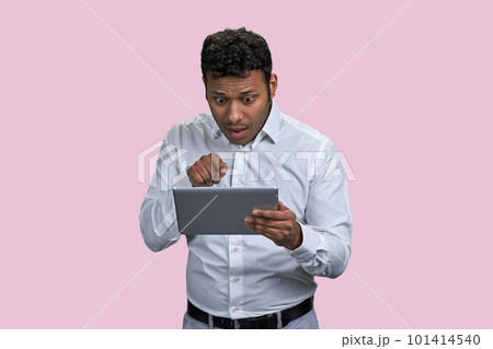 Shocked indian man pointing at someone on the tablet pc. Isolated on pink background. 101414540