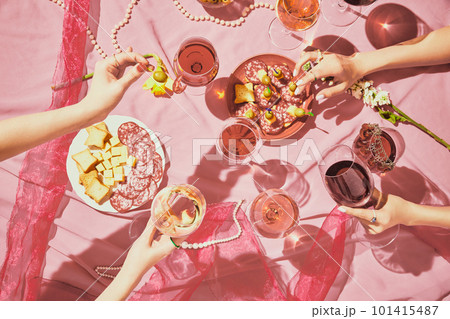 Hen party. Female hands with glassed with red and rose wine on pink textured background, tablecloth with appetizers, snacks 101415487