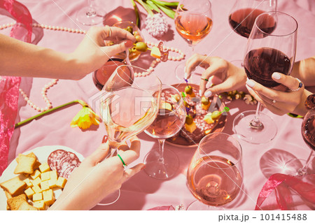 Holidays meeting. Female hands with glassed with red and rose wine on pink textured background, tablecloth with appetizers, snacks 101415488