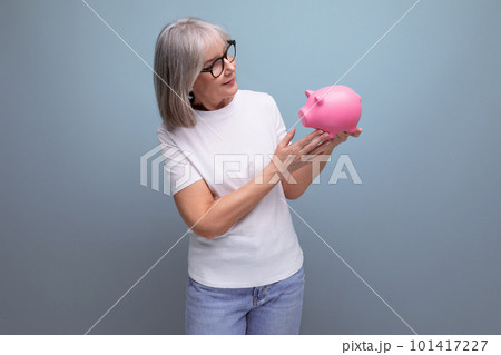 confident 60s woman with gray hair holding money capital with piggy bank on studio background with 101417227