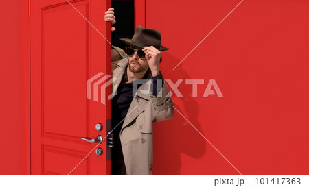 Stylish bearded man in trench coat and glasses, detective peeking out red door and attentively looking. Finding out secrets Stylish bearded man in trench coat and glasses, detective peeking out red door and attentively looking. Finding out secrets 101417363