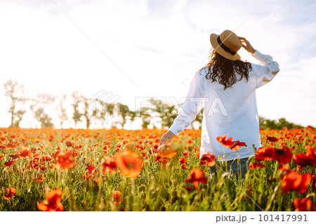 Young girl in hat posing in the poppy field. Portrait of curly girl walking in poppy field at sunset. Young girl in hat posing in the poppy field. Portrait of curly girl walking in poppy field at sunset. 101417991