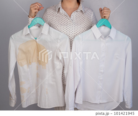 A woman compares two white shirts before and after washing. The girl is holding one blouse, clean and ironed, and the other, dirty with coffee stains 101421945