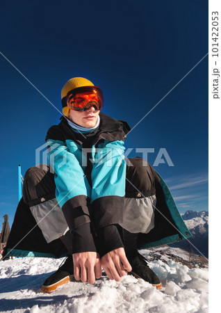 Man sitting on top of a hill. Young man squatting in warm clothes on a sunny day in the snowy mountains Man sitting on top of a hill. Young man squatting in warm clothes on a sunny day in the snowy mountains 101422053