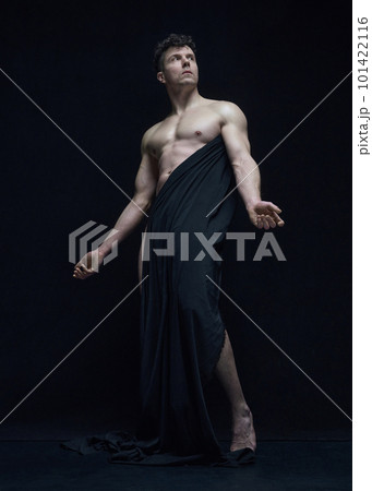 Full-length portrait of mature, handsome, shirtless man posing in dark fabric against black studio background 101422116