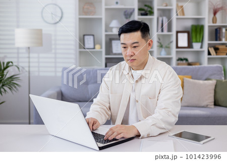 Serious and focused Asian man, businessman, freelancer, student working studying at home using laptop, Sitting at table and talking on video call, typing. 101423996