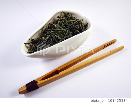 Dry Chinese green tea in a porcelain bowl and bamboo tongs. Tea ceremony Dry Chinese green tea in a porcelain bowl and bamboo tongs. Tea ceremony 101425334