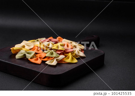Raw farfalle pasta in different colors on a dark concrete background Raw farfalle pasta in different colors on a dark concrete background 101425535