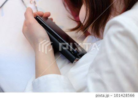 ベッドで寝ながらスマホを見ている女性 101428566