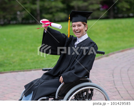 Caucasian woman in a wheelchair in a graduate costume rejoices at receiving a diploma. Caucasian woman in a wheelchair in a graduate costume rejoices at receiving a diploma. 101429585