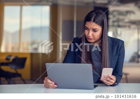 Serious businesswoman talking on mobile phone at office workplace, working at computer. Secretary answering telephone call. Serious businesswoman talking on mobile phone at office workplace, working at computer. Secretary answering telephone call. 101431616