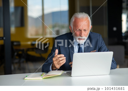 Handsome smiling senior man while sitting at his cozy workplace with laptop at home, retired male chatting with friends in social media, 101431681