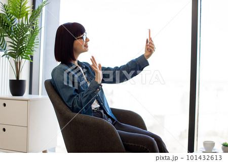 Woman sitting in office and using smartphone for video chat 101432613