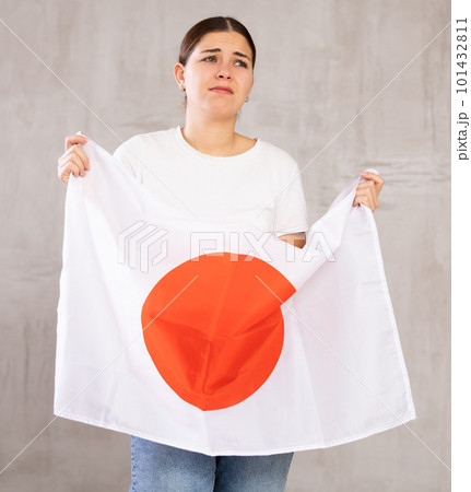 Disappointed young woman holding state flag of Japan against gray wall 101432811