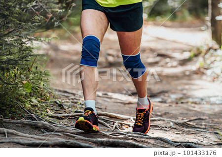 male runner in knee pads running forest trail on tree roots, summer marathon race 101433176