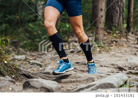 legs runner in compression sleeves on his feet run forest trail race over stones, summer marathon race 101433181