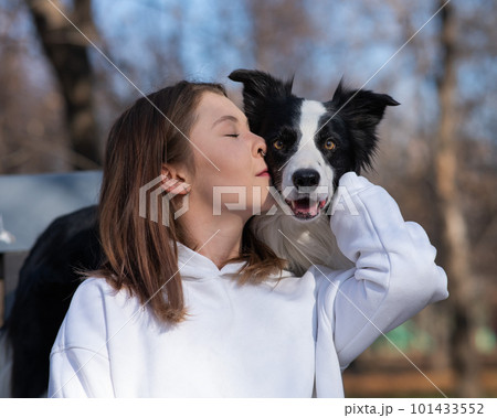 Caucasian woman hugging her dog Border Collie while sitting on a bench in autumn park. 101433552