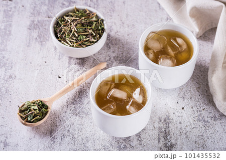 Iced green japanese hojicha tea in cups and leaves in a bowl on the table 101435532