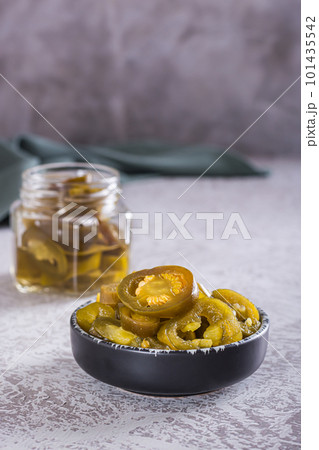 Sliced pickled jalapeno peppers in bowl and glass jar on table vertical view Sliced pickled jalapeno peppers in bowl and glass jar on table vertical view 101435542