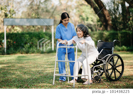 Asian careful caregiver or nurse and the happy patient in a wheelchair are walking in the garden to help and encourage and rest your mind with green nature. Help support yourself to learn to walk. 101436225