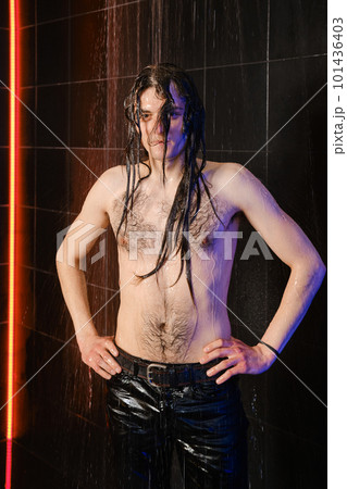 Handsome man with long hair and wet torso on a dark background in shower 101436403