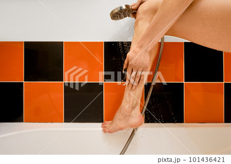 Unrecognizable woman put her foot on edge of bathroom and rinses it with water 101436421
