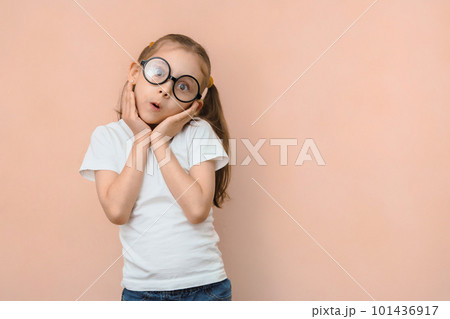 Cute surprised little caucasian girl in round glasses and hands near her face on a pink background with empty space Cute surprised little caucasian girl in round glasses and hands near her face on a pink background with empty space 101436917