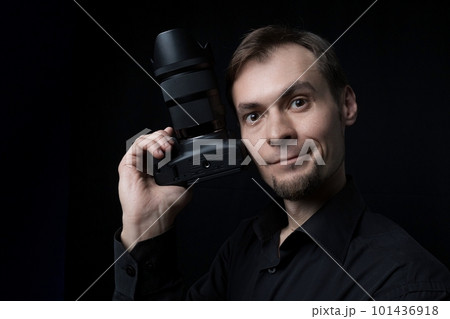 Low key close-up portrait of a professional photographer smiling man with black photo camera in hand 101436918