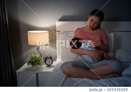 sleepy and tired mother breastfeeding newborm baby on bed at night sleepy and tired mother breastfeeding newborm baby on bed at night 101438309