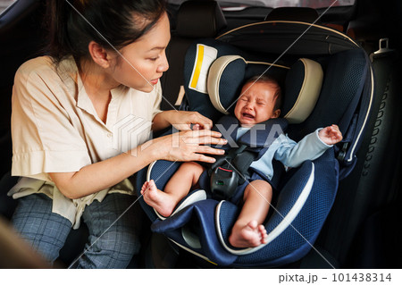 mother consoling her newborn baby crying while putting and fasten seat belts on car seat 101438314
