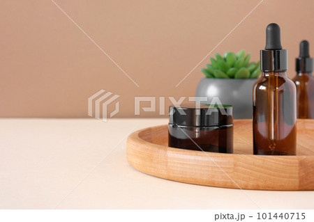 Glass bottles on wooden plate. Natural skin care SPA beauty product design. Mineral organic oil cosmetics on beige background. Earth tones. Mock-Up. Oily pipette. Face and body treatment. Front View 101440715