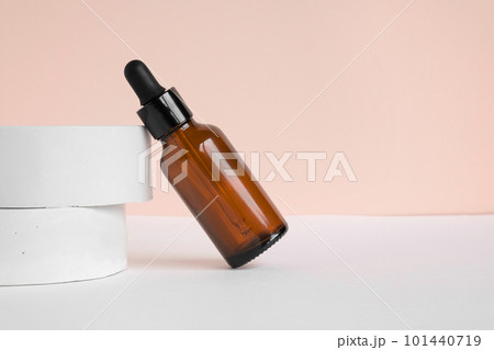 Amber glass dropper cosmetic bottle, white podium. Natural skin care SPA beauty product design. Mineral organic oil on beige background. Mock-Up. Oily pipette. Face and body treatment. Front view 101440719