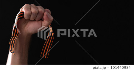 St. George's ribbon in a male hand on a black background with space for text 101440984